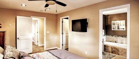 A bedroom with a bed, a ceiling fan, a TV, and a bathroom with a bathtub and shower.