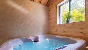Een hottub in een houten hutje, met uitzicht op bomen door het raam.