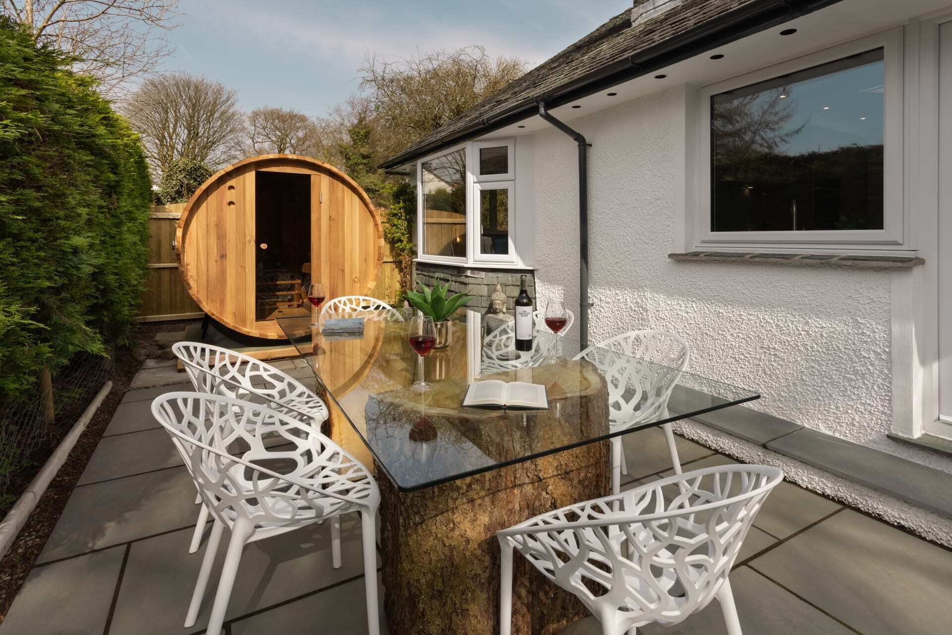 A wooden barrel-shaped structure with a glass table and white chairs in a garden setting.