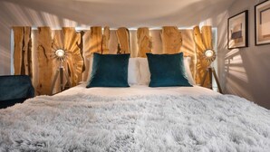 Een slaapkamer met een groot bed, een houten hoofdbord, twee bedlampen en een zacht, wit vloerkleed.