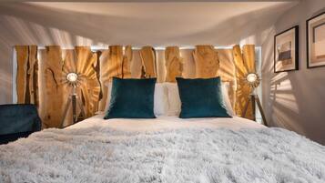 Un dormitorio con una cama grande, cabecera de madera, dos lámparas de noche y una alfombra blanca y mullida.