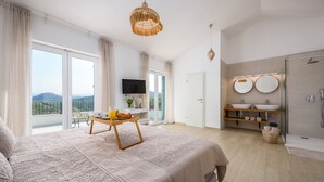 Un dormitorio amplio con una cama grande, una mesa de desayuno, un televisor y un baño con ducha y lavamanos.