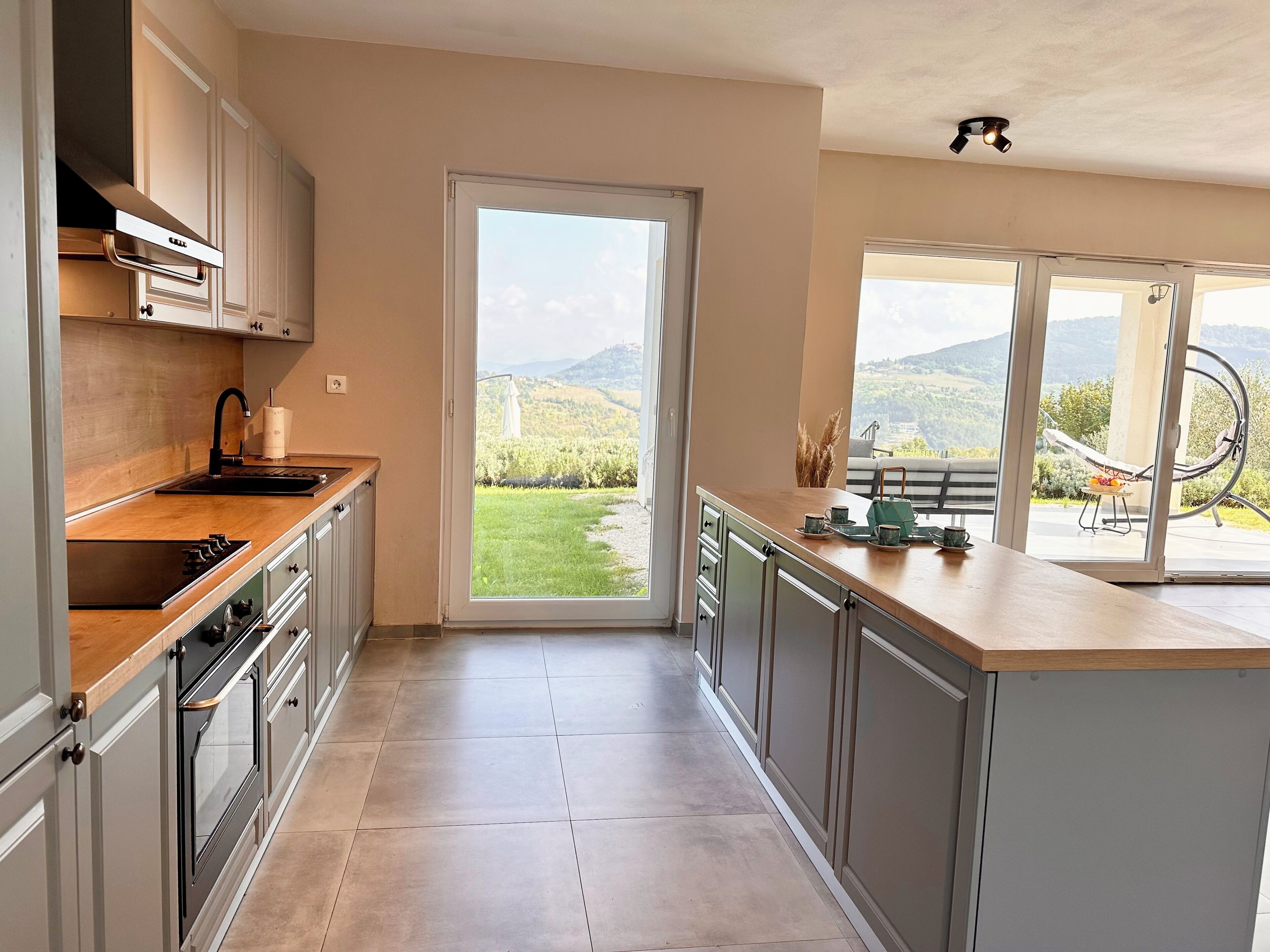 A modern kitchen with a large window, a built-in oven, and a view of a lush garden.