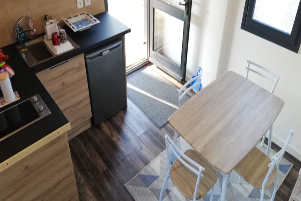 Eine kleine Küche mit schwarzem Arbeitsplatz, Holzschränken, einem Geschirrspüler und einem Essbereich mit Holztisch und weißen Stühlen.