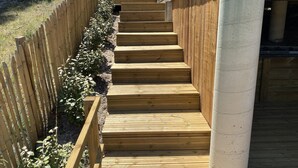 Una escalera de madera con una valla de madera a un lado y un pilar de concreto al otro.