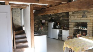 Eine Küche mit Steinwänden, Holzbalken, einem Herd, einem Kühlschrank und einem Esstisch mit Tischdecke.
