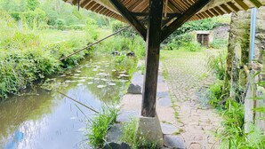 Eine rustikale Holzhütte mit Steinfundament, einem Kopfsteinpflasterweg und einem kleinen Gewässer mit Seerosenblättern.