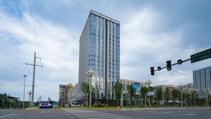 Un moderno edificio de gran altura con fachada de vidrio, situado en una intersección urbana con semáforos y paso de peatones.