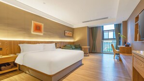 Una habitación de hotel moderna con una cama grande, cabecera de madera, un escritorio pequeño y vistas al exterior a través de un ventanal.