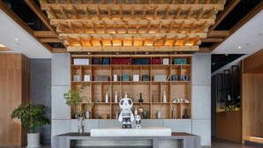 Un área de recepción con techo de madera, una estantería con diversos objetos y una figura de panda sobre una consola.