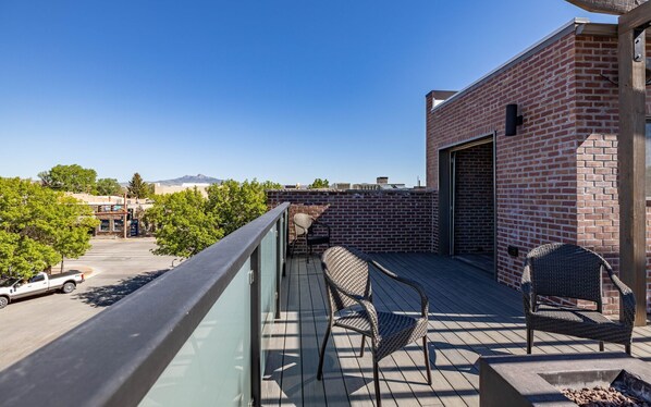A rooftop patio with two wicker chairs, a fire pit, and a view of a cityscape and mountains in the distance. - Downtown Loft- Great downtown Location with Rooftop Deck and Modern Interior (Cody)