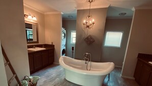 Ein geräumiges Badezimmer mit freistehender Badewanne, einem Doppelwaschbecken, einer Waschmaschine und einer Chandelier.