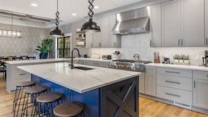 A modern kitchen with a central island, bar stools, stainless steel appliances, and a herringbone-patterned backsplash. - Luxury Property: Private Pool, Hot Tub, Fire Pit and Close to Lake Sunsets (Fennville)