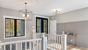 A spacious hallway with a wooden floor, white railings, and a view of the outdoors through large windows. - Luxury Property: Private Pool, Hot Tub, Fire Pit and Close to Lake Sunsets (Fennville)