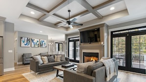 A spacious living room with a fireplace, a ceiling fan, and a large window overlooking a deck. - Luxury Property: Private Pool, Hot Tub, Fire Pit and Close to Lake Sunsets (Fennville)