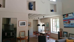 Un vaste espace de vie doté d’un haut plafond, une table à manger avec des chaises, une cuisine équipée d’une cuisinière et une grande fenêtre laissant entrer la lumière naturelle.