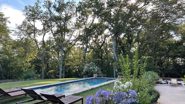 Une piscine rectangulaire entourée d’une terrasse en bois avec des chaises longues.