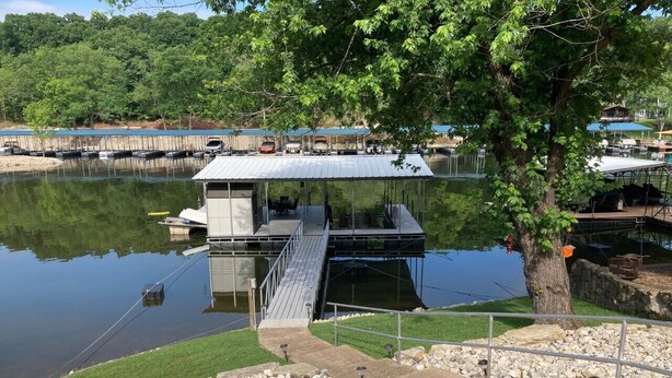 A docked boat with a covered deck, a small bridge leading to a dock, and a tree in the foreground. - Lake front home, 10mm, dock, only steps to the water, close to Franky & Louies (Sunrise Beach)