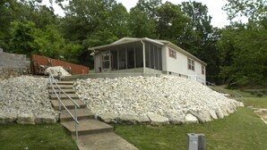 A house with a porch, a stone retaining wall, and a concrete pathway leading to the entrance. - Lake front home, 10mm, dock, only steps to the water, close to Franky & Louies (Sunrise Beach)