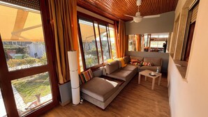 A cozy living room with a sofa, a small table, and a lamp. Large windows allow natural light and views of the outdoors. - Julia House (Viareggio)