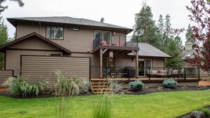 Una casa a due piani con veranda coperta, garage e giardino curato con rocce e piante.