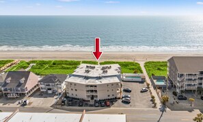An aerial view of a coastal hotel with a parking lot, beach access, and ocean views.