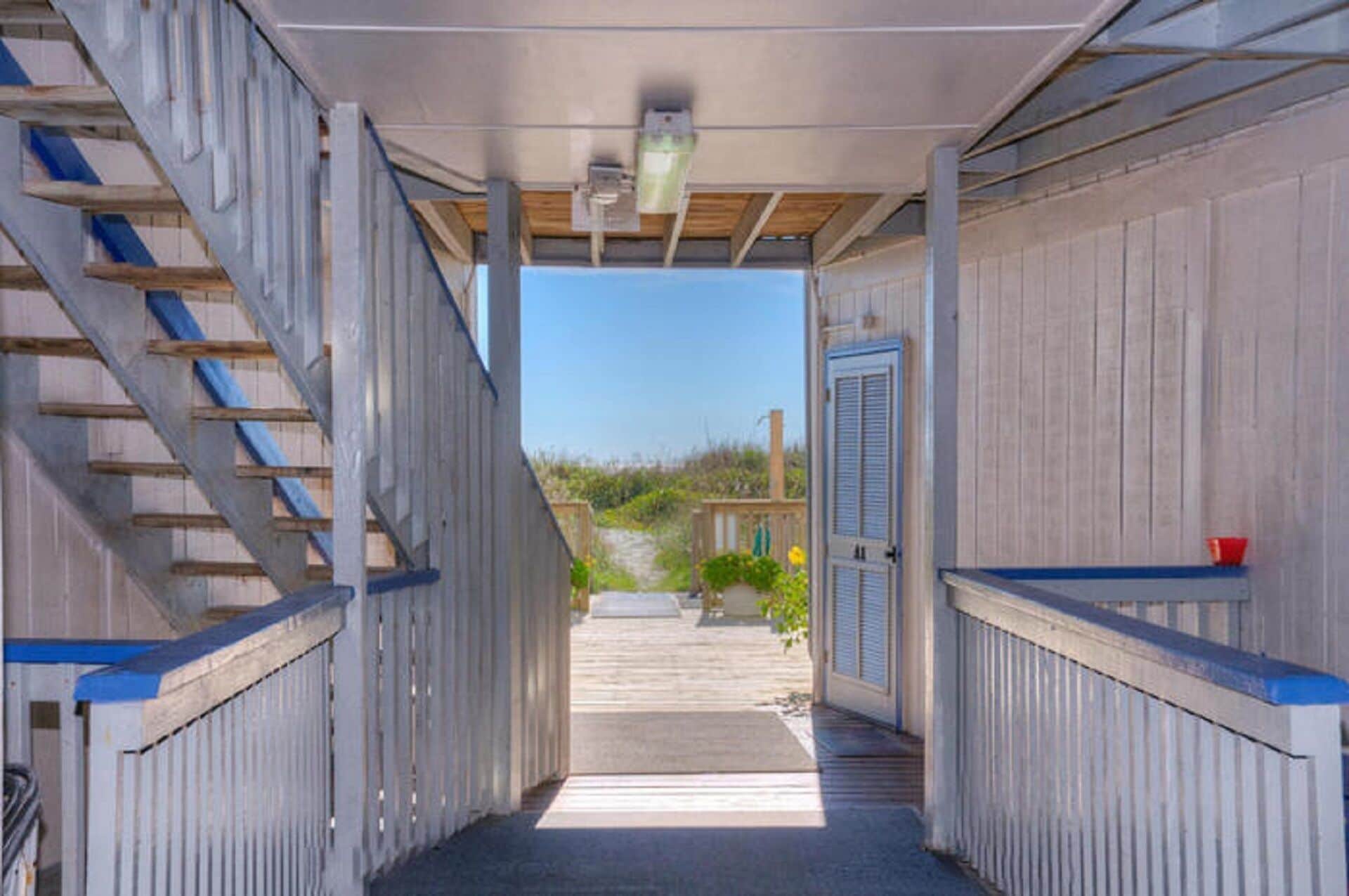 A covered walkway leading to a beach house with a wooden exterior and a view of the beach.