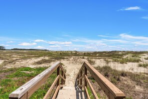 A wooden boardwalk leading to a beach with dunes and a clear sky.