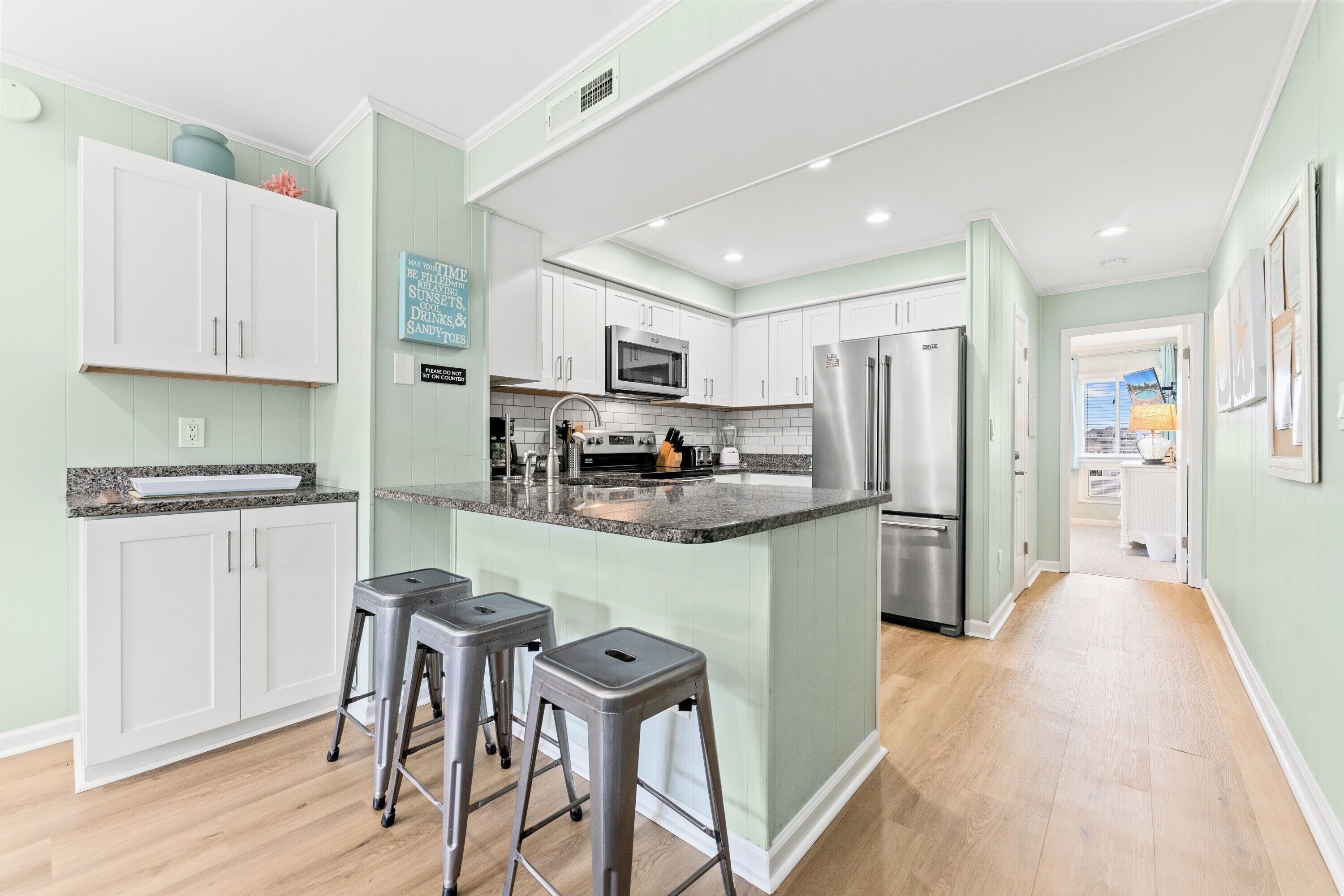 A modern kitchen with white cabinets, a stainless steel refrigerator, and a granite countertop.