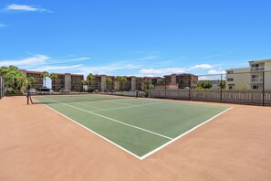 A tennis court with a net, surrounded by buildings and a fence.