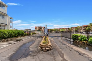 A gated entrance to a residential area with a stone planter in the center, a clear sky, and a fence with a sign.