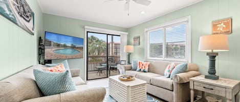 A living room with a pool view, a ceiling fan, and a beach-themed sign.