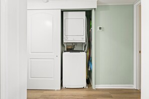 A compact laundry room with a washing machine and dryer, a small heater, and a door leading to a hallway with a green wall.