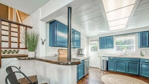 Eine Küche mit blauen Schränken, einer Holztischinsel, einer Kaffeemaschine und Blick ins Freie.