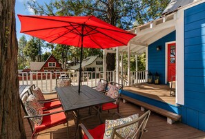 A covered outdoor seating area with a table and chairs, a red umbrella, and a blue building in the background.