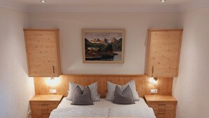 A bedroom with a bed, wooden headboard, bedside tables, a painting, and a wooden dresser. - Cozy vacation apartment between Moselle and Rhine, near various dream loops and castles (Brodenbach)