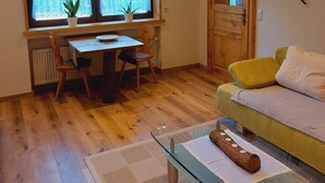 A cozy room with a wooden floor, a dining table with chairs, a sofa, a radiator, and a window with lace curtains. - Cozy vacation apartment between Moselle and Rhine, near various dream loops and castles (Brodenbach)
