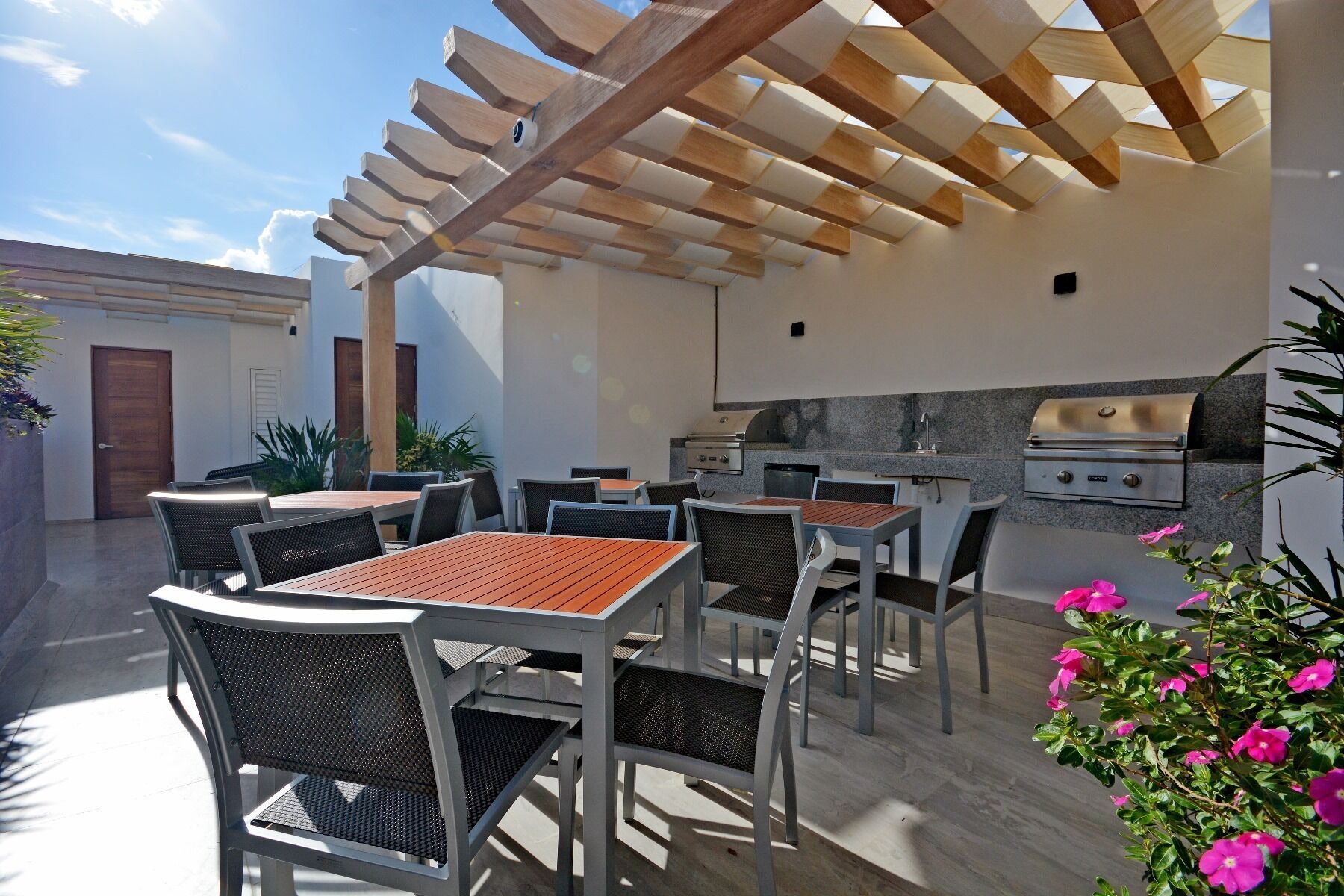 An outdoor patio with tables and chairs, a pergola, and a built-in grill station.