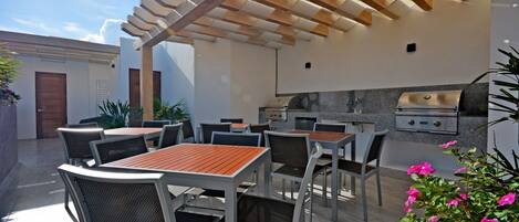 An outdoor patio with tables and chairs, a pergola, and a built-in grill station.