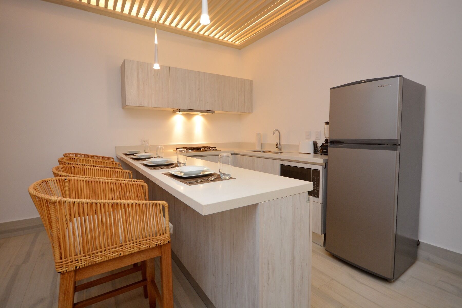 Una cocina moderna con una isla central, refrigerador de acero inoxidable y sillas de mimbre.