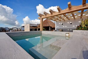 A modern pool area with a clear pool, wooden pergola, and a thatched-roof structure. - Mayan Monk (Playa del Carmen)