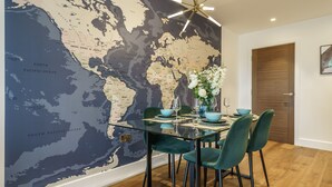 Un coin repas avec une table en verre, des chaises de couleur turquoise et une fresque représentant une carte du monde sur le mur.