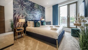 Une chambre moderne avec un grand lit, une table de chevet, un téléviseur fixé au mur et une grande fenêtre avec des rideaux.