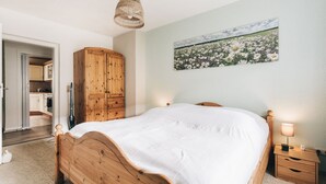 A bedroom with a wooden bed, a nightstand, a wall-mounted lamp, and a painting of a flower field.