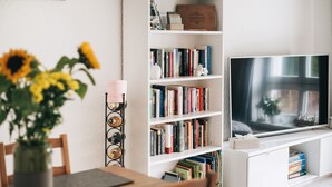 A living room with a TV, bookshelf, and a vase with flowers.