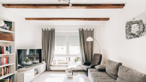 A modern living room with a flat-screen TV, bookshelves, a sofa, and a window with curtains.