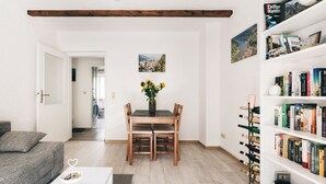 A modern living room with a wooden dining table, a bookshelf filled with books, and a vase with sunflowers.