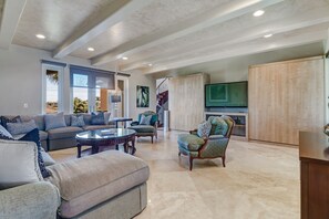 A spacious living room with a large sofa, armchairs, a coffee table, and a TV.