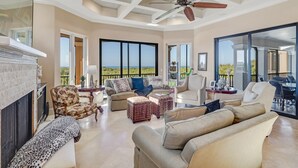 A spacious living room with a fireplace, comfortable seating, and large windows offering a view of the outdoors. - Southern Charm Close To Beach (Marco Island)