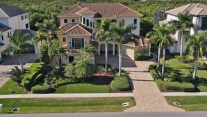 A large, two-story house with a tiled roof, surrounded by well-maintained lawns and palm trees. - Southern Charm Close To Beach (Marco Island)